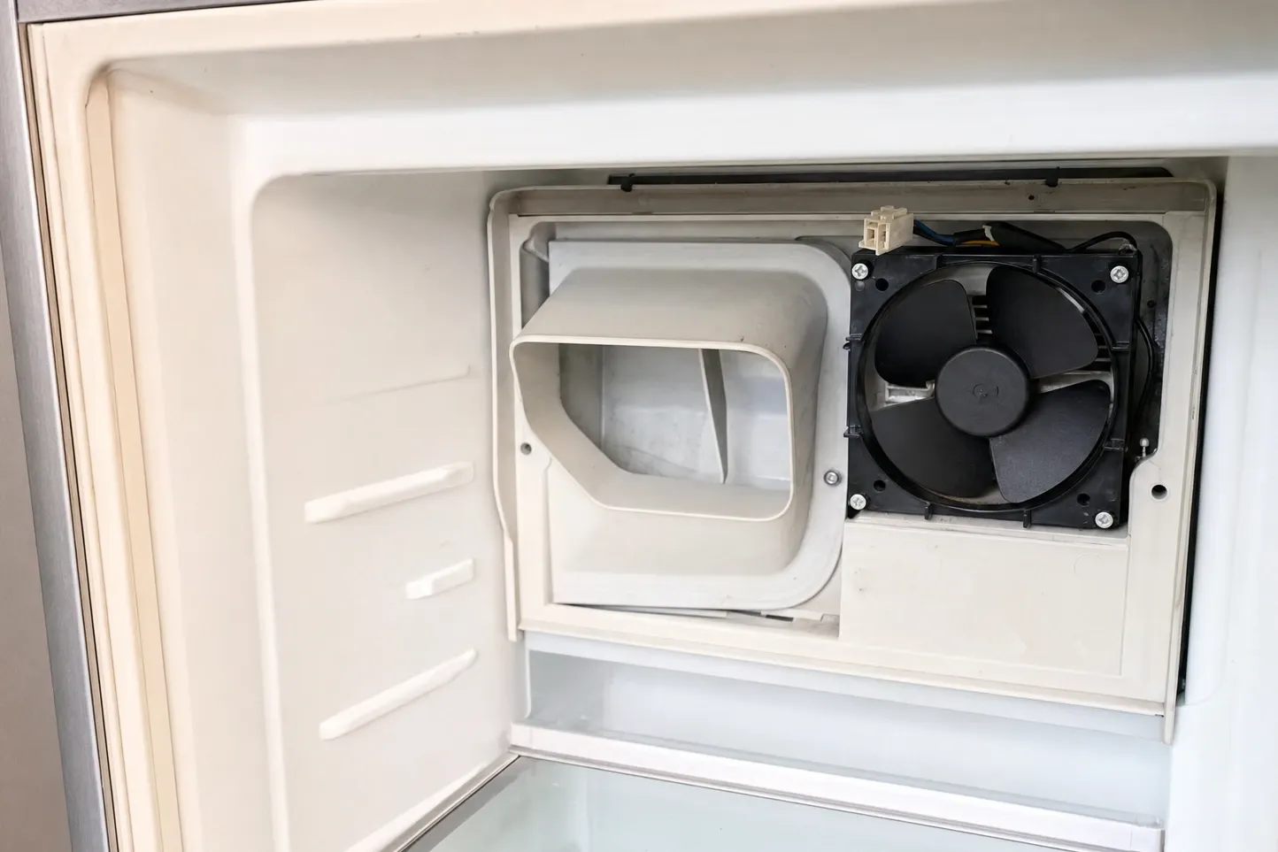 Freezer compartment with the rear cover removed, exposing the evaporator fan on its bracket and the moulded air duct